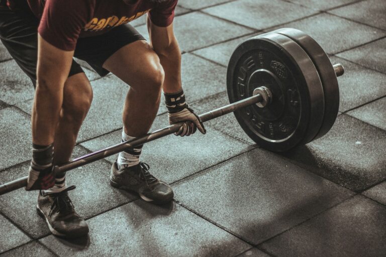 Person preparing to deadlift barbell in gym showing muscular legs and proper lifting form