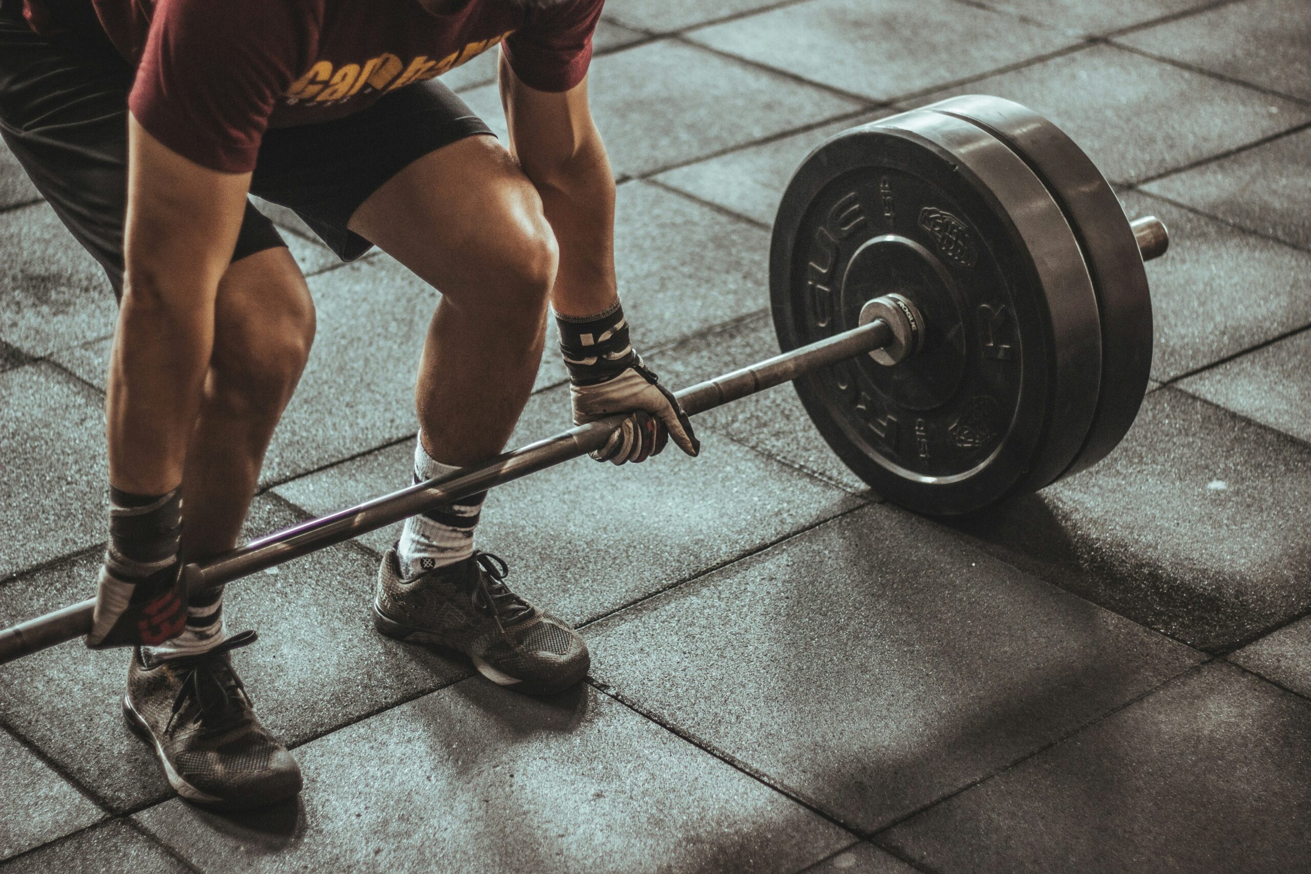 Person preparing to deadlift barbell in gym showing muscular legs and proper lifting form