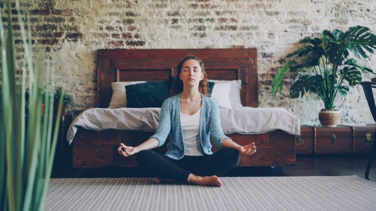 Woman sitting peacefully on bedroom floor with eyes closed practicing mindfulness