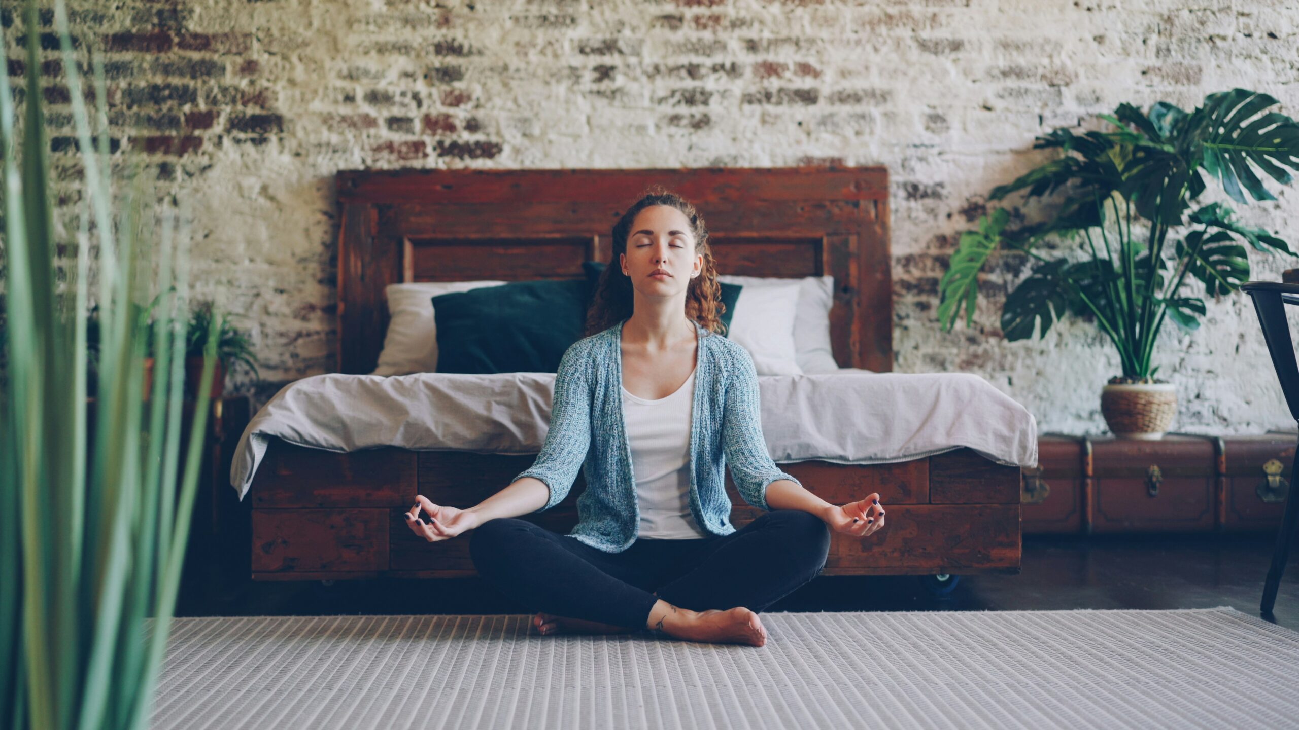 Woman sitting peacefully on bedroom floor with eyes closed practicing mindfulness